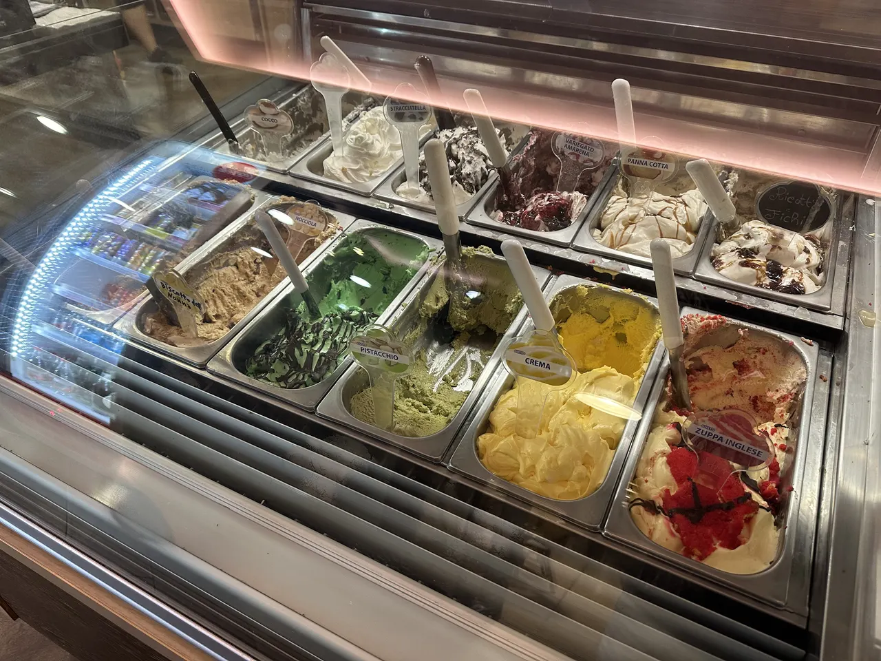 La vetrina del gelato artigianale: vaschette di pistacchio, crema, fragola e cioccolato sotto la luce rosa